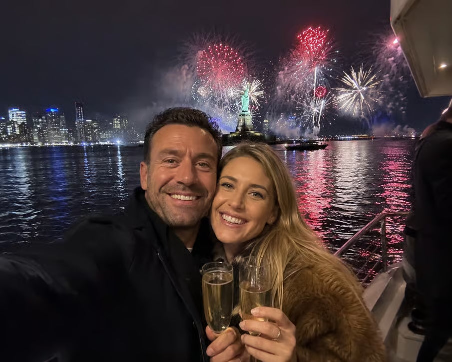 Couple celebrating New Year's Eve with champagne and fireworks behind Statue of Liberty on NYC cruise