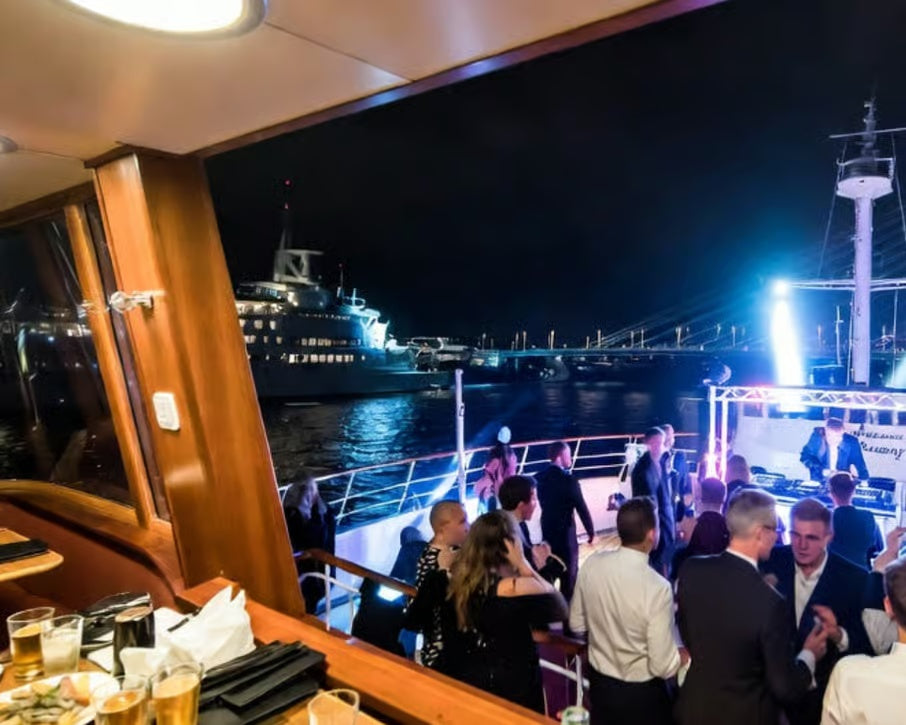 Guests enjoying a New Year's Eve DJ party aboard a boat in Rotterdam with city lights outside
