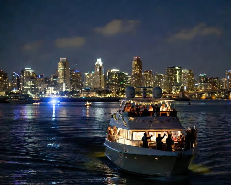 Illuminated yacht with passengers sailing in San Diego Bay against the downtown skyline at night